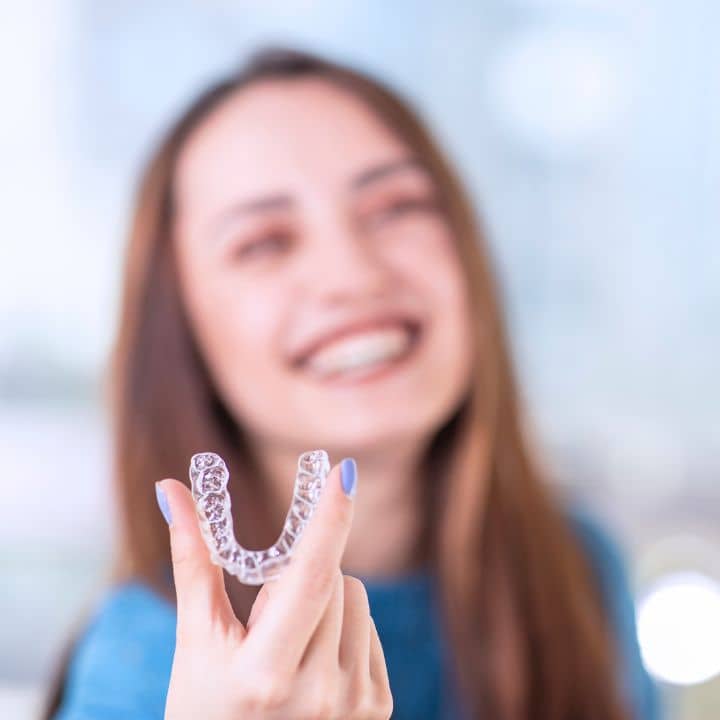 En person ler medan han håller i en genomskinlig dental aligner, med en suddig bakgrund som påminner om tandläkare Örnsköldsvik.